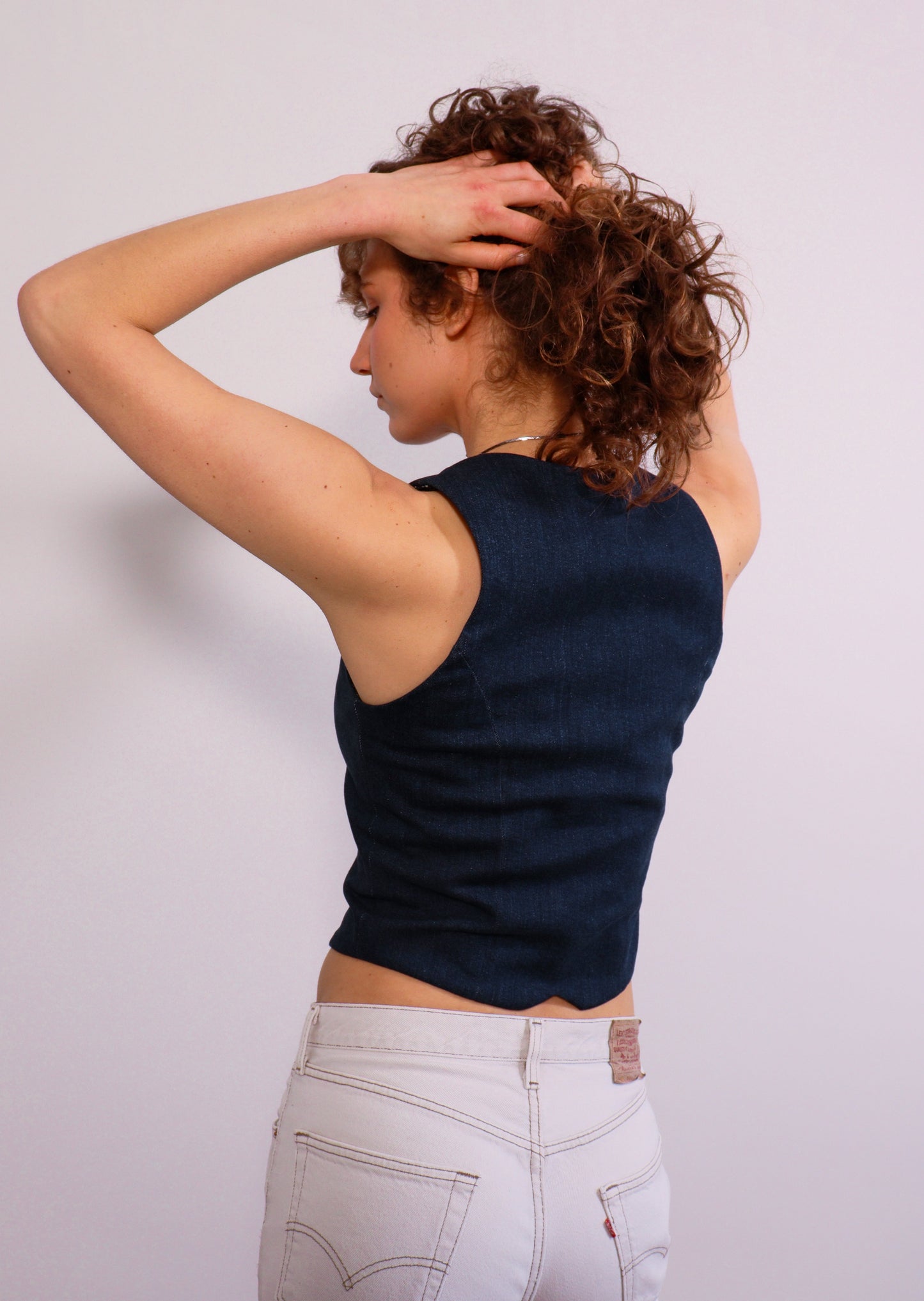 Back view of the denim vest with flattering seams that follow the garment.